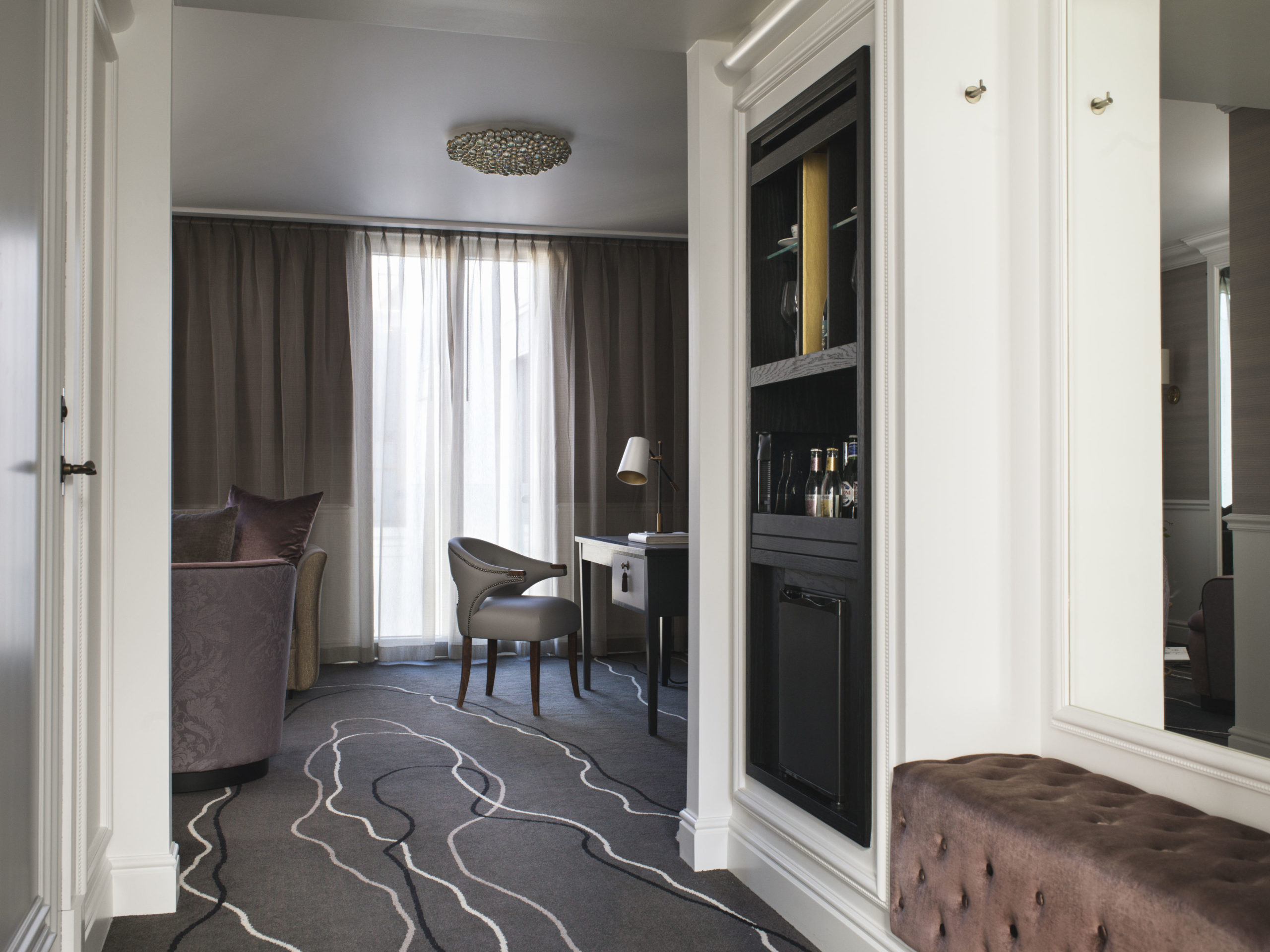 Deluxe room, entrance with a seating bench, large mirror and wine cabinet