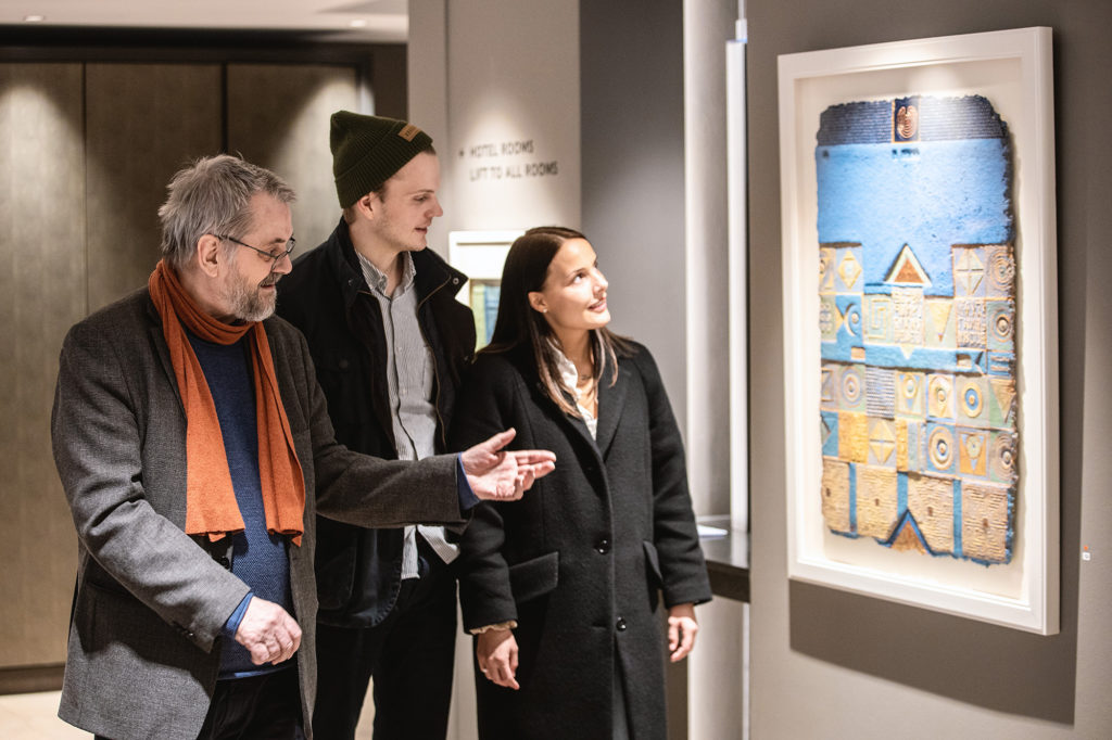 a young couple examine a piece of artwork by Arnold Dahlslett in Britannia Hotel, accompanied by the artist himself