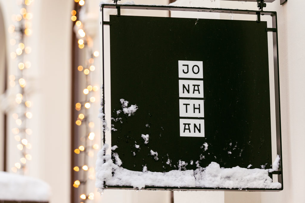 Jonathan grill sign in the snow with Christmas lights behind outside